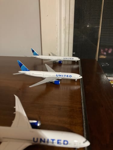 Reviewer's HERPA UNITED 777-200 model airplane in the new blue livery, displayed next to other United models on a table.