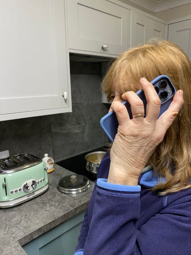 Customer holding their blue-cased Apple iPhone 13 Pro to their ear while on a call.