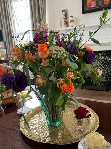 Customer's vibrant Loose and Lovely Flower Arrangement in a teal vase on a table with a cupcake and single red rose.