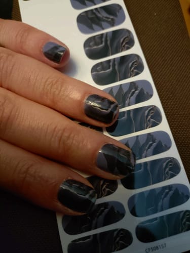 Hand einer Kundin mit aufgetragenen Winter Rose Nagelfolien neben dem unbenutzten Bogen.