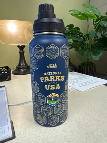 Customer's blue Lets Wander™ National Parks Water Bottle on a desk, with one colorful sticker placed over a gold hexagon.