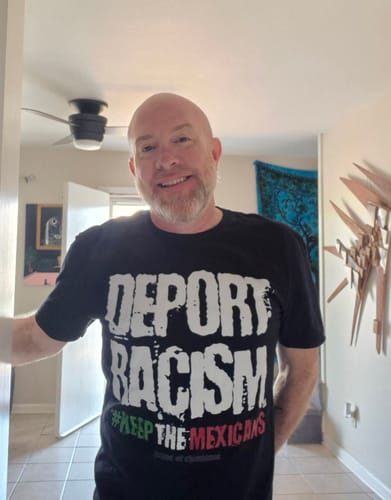 A smiling customer wearing the black 'Deport Racism' t-shirt indoors.