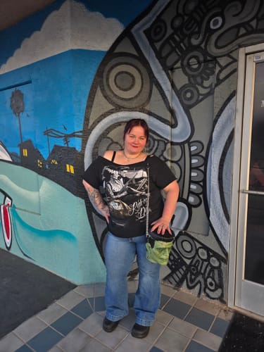 Reviewer standing in front of a mural and holding a green Frankenstein-head shaped purse.