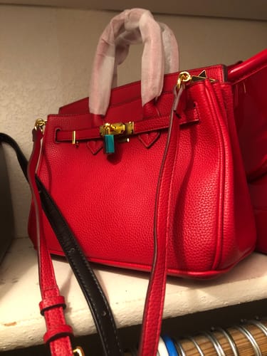 Reviewer's bright red Warkin Bag on a shelf. The pebbled leather bag has its handle wrapped and a prominent gold lock closure.