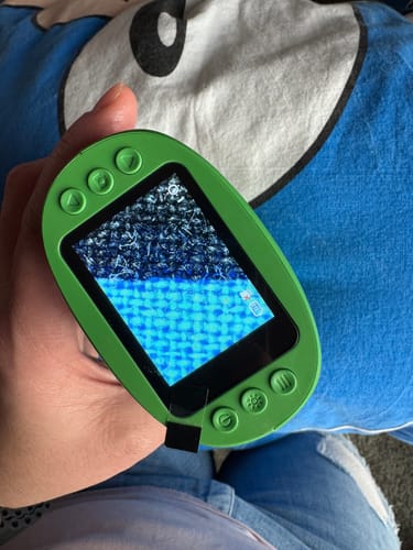 Ein Kunde hält das grüne Abenteuer-Mikroskop in der Hand, der Bildschirm zeigt eine stark vergrößerte, blau texturierte Oberfläche.