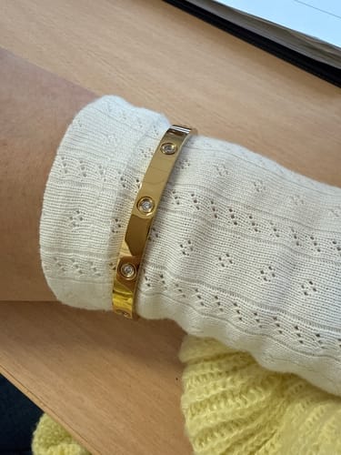 Rezensentin trägt ein glänzendes goldenes Armband mit Steinen am Handgelenk über einem weißen Pulloverärmel.
