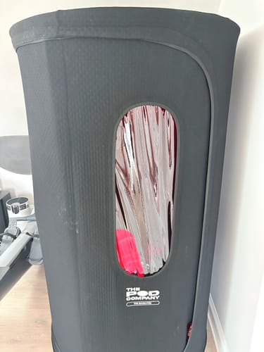 A customer's black Sauna Pod 2.0 set up in a room, with a window showing the reflective silver interior.