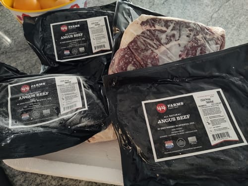 Reviewer's four vacuum-sealed USDA Prime Chuck Roasts on a counter. One package shows the raw, marbled meat.