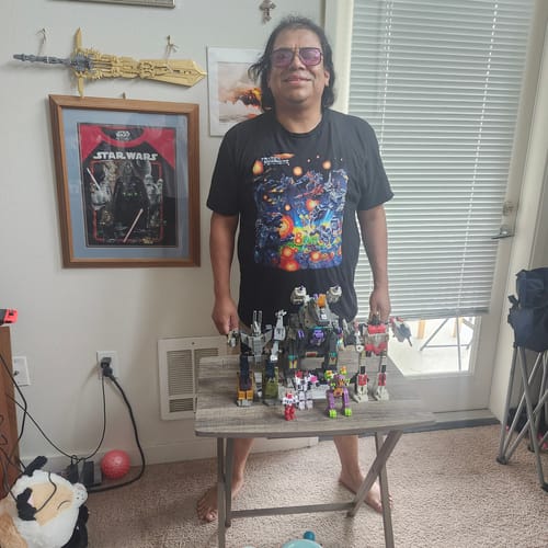 Customer wearing the black Con Package Transformers T-Shirt while standing in a room with Transformers toys.