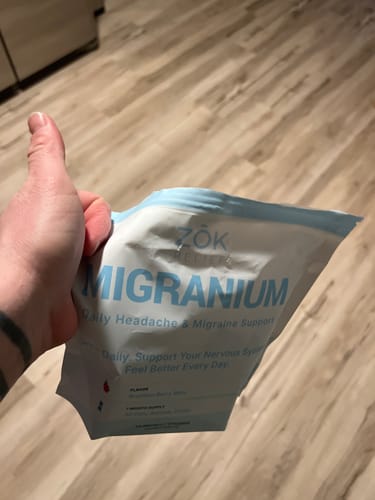 Reviewer holding a pouch of Migranium supplement and giving a thumbs-up.