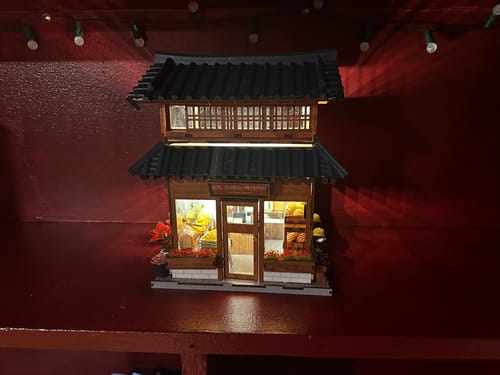 Customer's finished Hanok Bakery miniature kit. The detailed, two-story building is lit from within and displayed on a shelf.