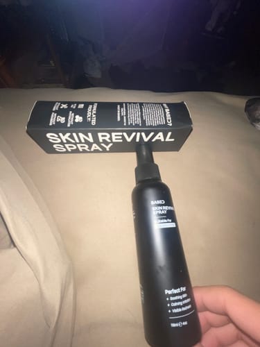 Customer holding the black Skin Revival Spray bottle with the product's box balanced on top of it.