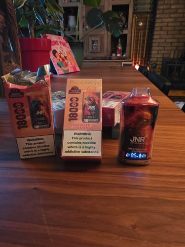 Customer's unwrapped JNR Falcon X vape with its screen on, next to several product boxes on a wooden table.