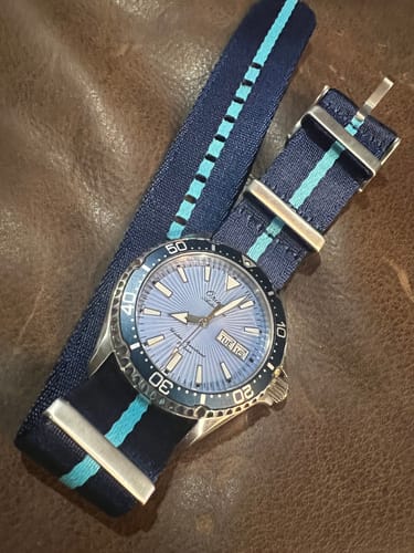 Customer's Orient Kamasu dive watch with the striped AlphaPremier - Blu Moon watch strap laid on a brown leather surface.