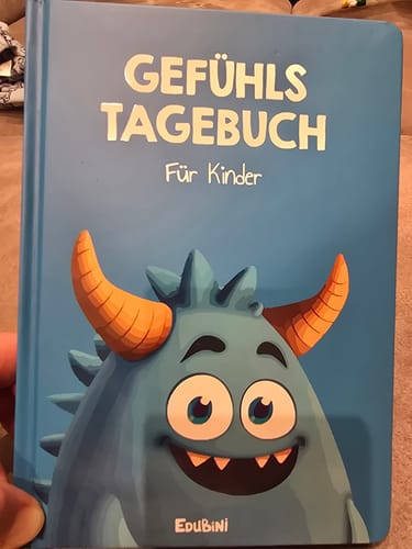 Rezensent hält das hellblaue Gefühlstagebuch für Kinder, das ein freundliches blaues Monster auf dem Cover zeigt.