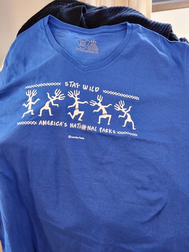 Customer's blue Stay Wild Petroglyphs V-Neck Tee, showing the white graphic of petroglyph figures and text.