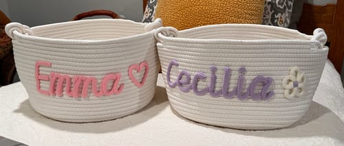 Customer's two personalized white rope baskets, one with the name 'Emma' in pink and a heart, the other with 'Cecilia' in purple and a flower.
