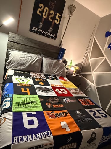 Customer's colorful Premium T-Shirt Quilt, made from various sports jerseys, neatly spread across a bed in a bedroom.