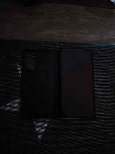 Kunde zeigt sein Samsung-Handy mit aufgebrachter Schutzfolie in einer geöffneten, schwarzen Klapphülle.