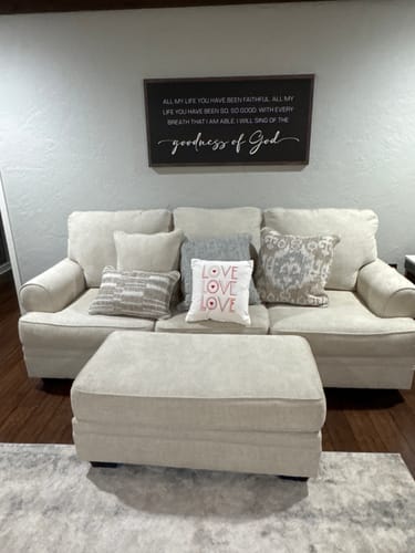 Reviewer's Goodness Of God Faith Sign II hanging on a wall above a light-colored sofa in their den.
