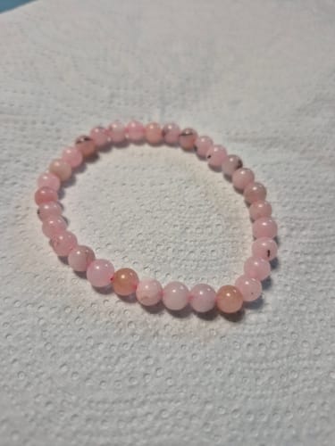 Photo d'un client montrant le bracelet en opale rose à perles rondes posé sur une surface blanche.