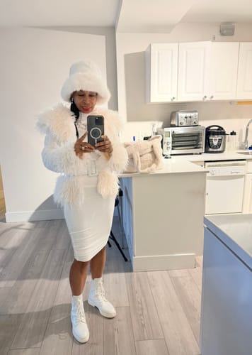 Reviewer taking a mirror selfie in a kitchen wearing the white Sherpa Faux Fur Jacket with a matching skirt and hat.