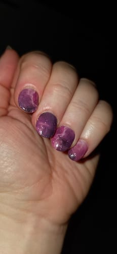 Die Hand einer Kundin zeigt die glitzernden 'Pink Nebula' UV-Gelfolien nach zwei Wochen Tragezeit.