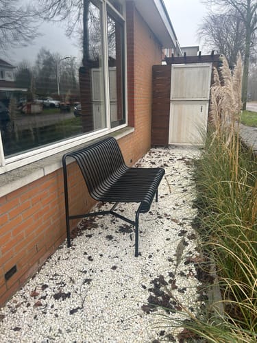 De antracietkleurige HAY Palissade tuinbank van een recensent, buiten op een pad van witte kiezels geplaatst.