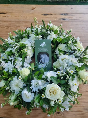 Customer's Heavenly Grace White Wreath on a wooden table with a custom memorial card placed in the center.