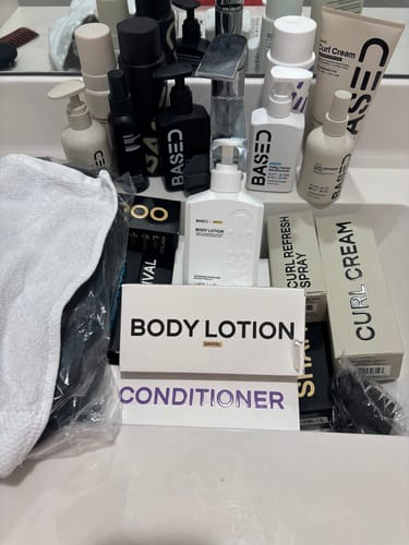 Customer's white bottle of Body Lotion in a bathroom sink filled with many other hair and body care products from the same brand.