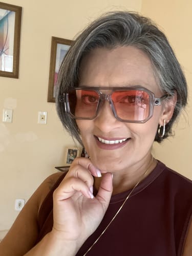 Cliente sorrindo e usando os Óculos Villanova com armação translúcida e lentes avermelhadas.