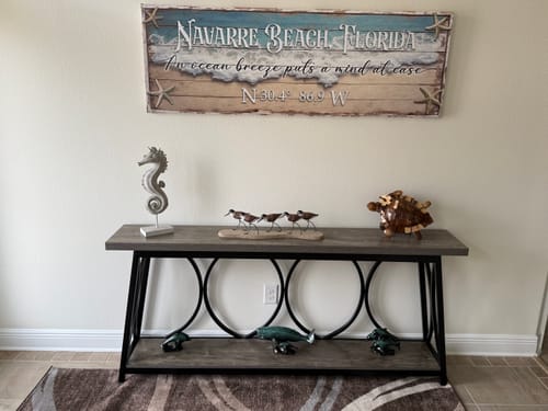 Reviewer's personalized coastal sign with 'Navarre Beach Florida' text hanging on a wall over a console table.