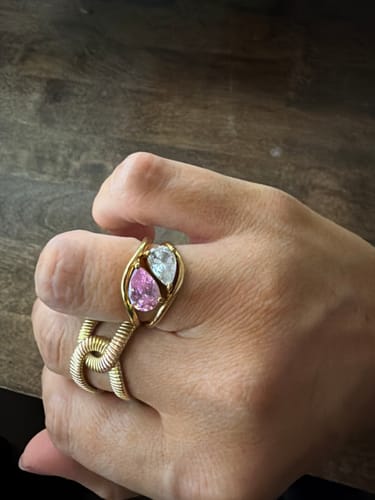 Customer's hand wearing two stacked Pia Birthstone Rings, one with a pink stone and the other with a clear one.