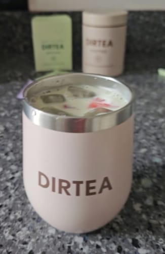 Customer's iced strawberry DIRTEA Matcha served in a pink branded tumbler, with DIRTEA packaging in the background.