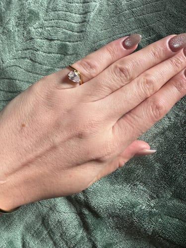 Close-up of a reviewer's hand wearing the gold Pia Ring, showing the pear-cut stone and sleek wave band.