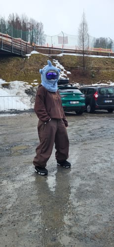Reviewer wearing the baggy coffee snow pants while standing on wet ground in a snowy area.