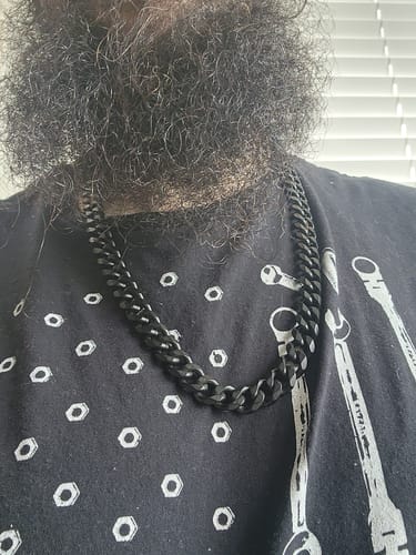 Customer wearing the matte black Never Retreat Alpha Wolf Cuban Link Necklace against a patterned t-shirt.