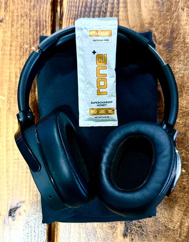Customer's packet of Caffeine-Free SuperCharged Honey resting against a pair of black headphones on a wooden surface.