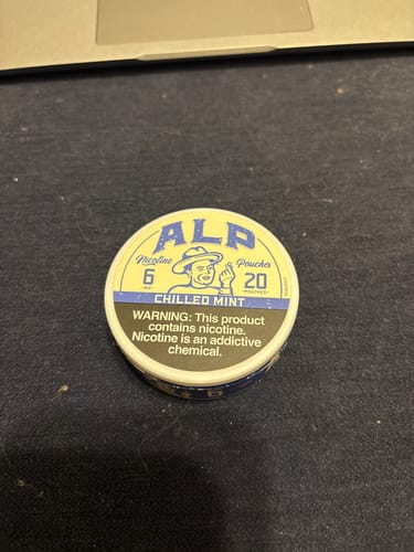 Customer's round tin of ALP Chilled Mint Nicotine Pouches sitting on a dark surface.