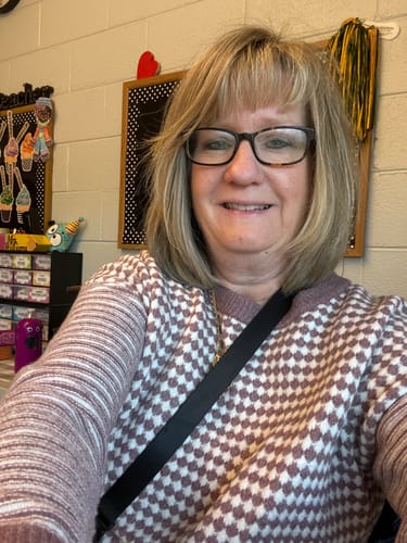 Reviewer in a classroom wears the Mixed Prints Ribbed Trim Sweater, showing its mauve checkered body and striped sleeves.