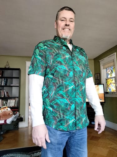 Reviewer wearing the vibrant green Predator "I See You" shirt with a dense jungle pattern.