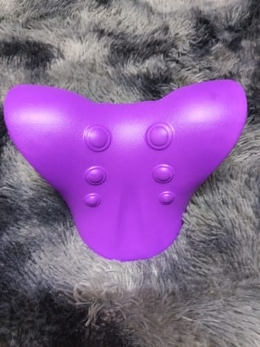 A vásárló lila Kiropraktikus Nyak- és Váll Lazító Párnája egy puha, szürke szőnyegen.