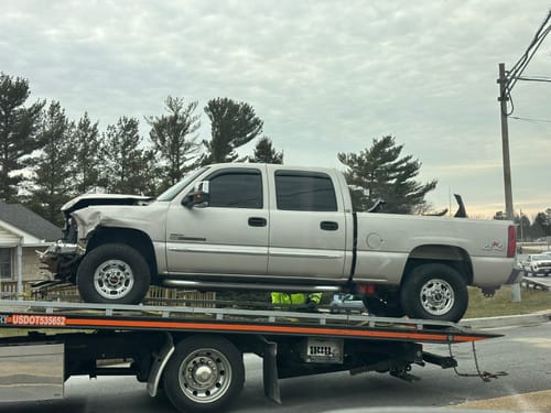 Reviewer's damaged silver truck with a crumpled front end, shown on the back of a tow truck.