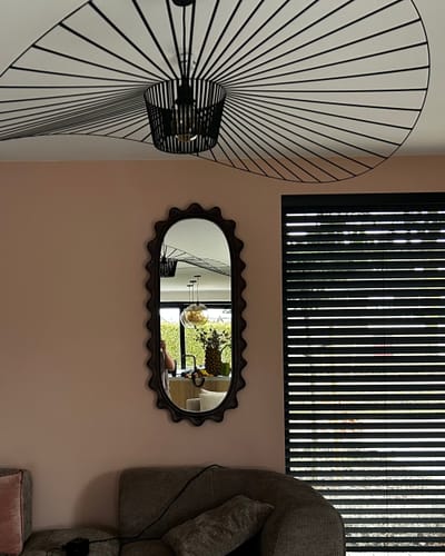 Recensent's ovale HKliving Ripple spiegel met een golvende, donkere lijst in een interieur.