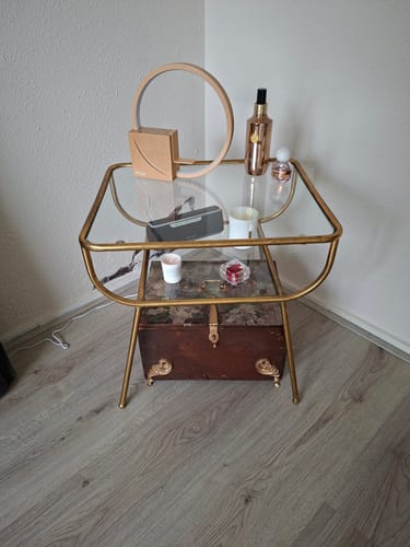 Klant toont de WOOOD Amazing bijzettafel met messing frame en glazen planken, gestyled in een hoek van een kamer.