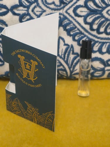 Reviewer's small sample vial of Honeyberry fragrance next to its branded dark green card holder.