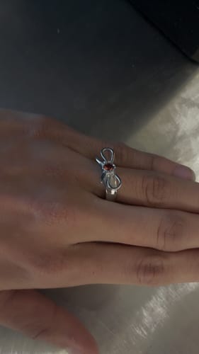 Customer's hand wearing the RING OF REPUTATION, showing the silver bow design with a reddish central stone.