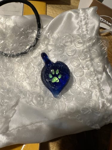 Customer's repaired heart-shaped pendant made of blue glass with a glowing green paw print in the center.