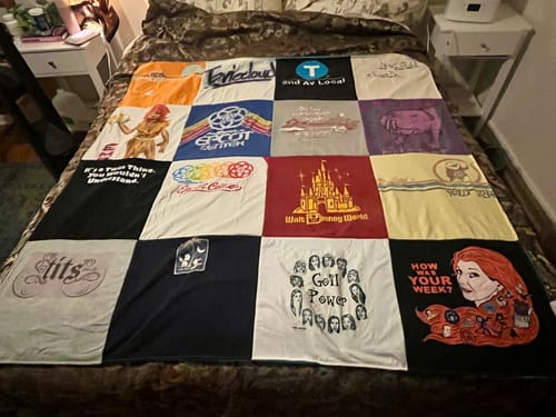 A reviewer's finished Premium T Shirt Quilt spread out on a bed, showing a colorful patchwork of various graphic t-shirts.