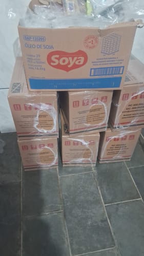 Cliente mostra as caixas da Cesta Básica Econômica Kit empilhadas em um piso escuro.